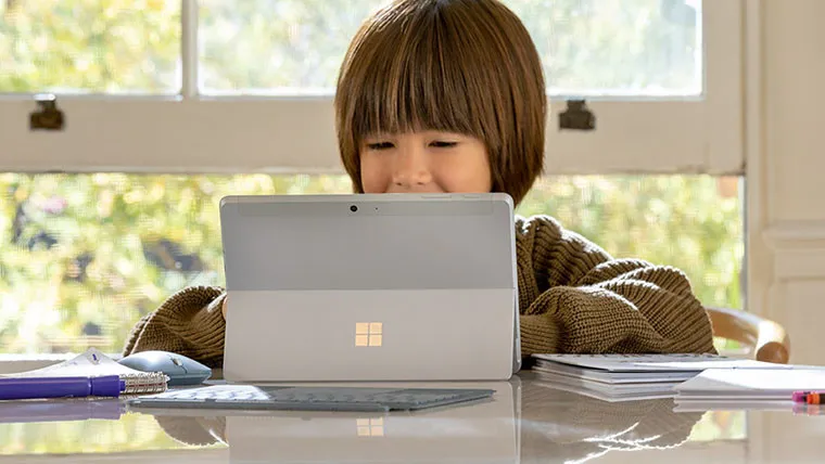 Parte de trás de um Surface Go 2 em pé sobre uma mesa e sendo usado por uma criança