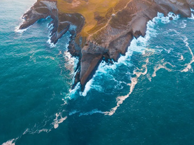 シアンの海と泡立つ波のある岬の航空写真