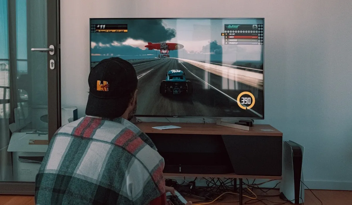 Persona che gioca con la PS5 su una TV a schermo piatto posizionata su un supporto marrone