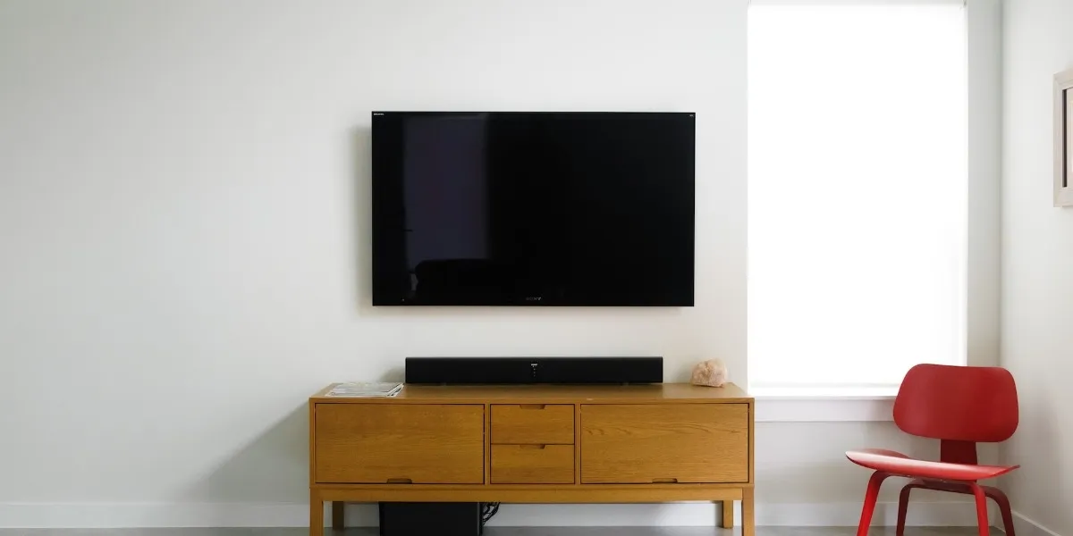 TV a grande schermo sulla parete bianca con un supporto TV marrone e una sedia rossa