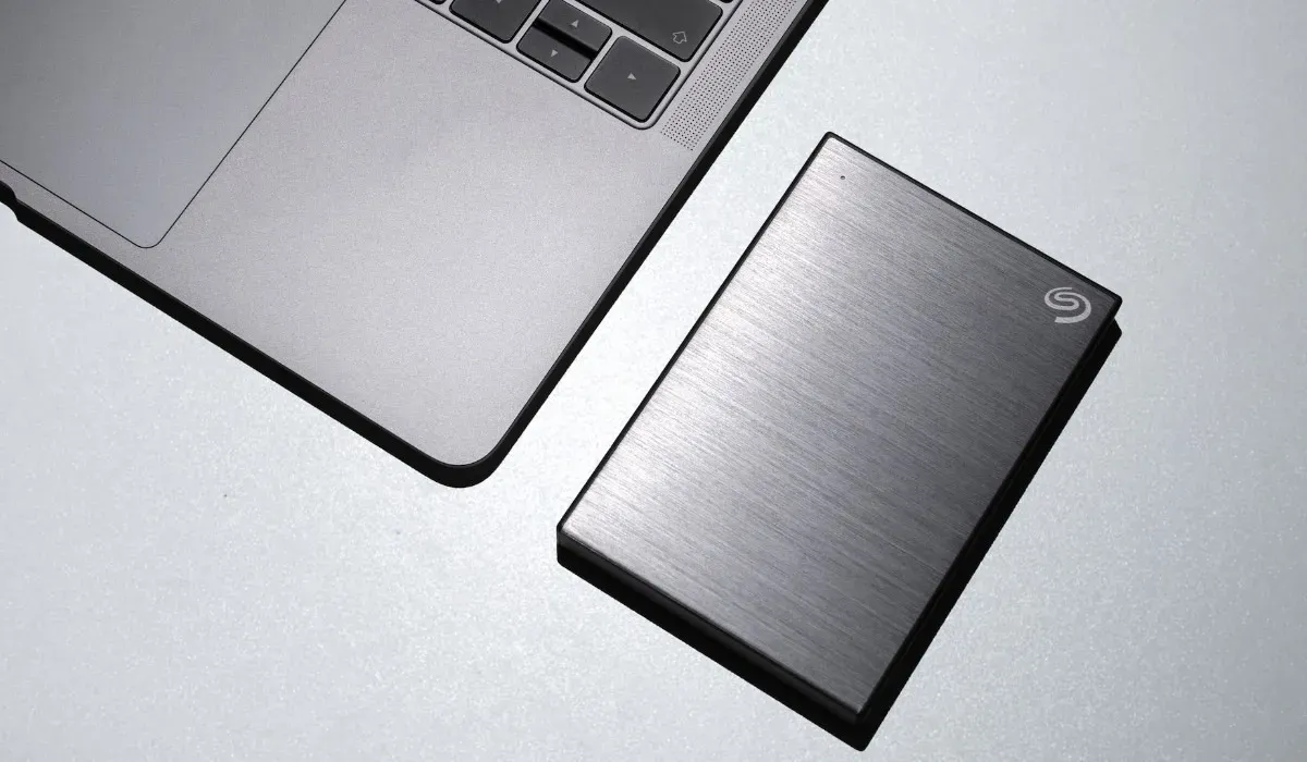 Disco rigido esterno nero su una superficie bianca accanto a un laptop