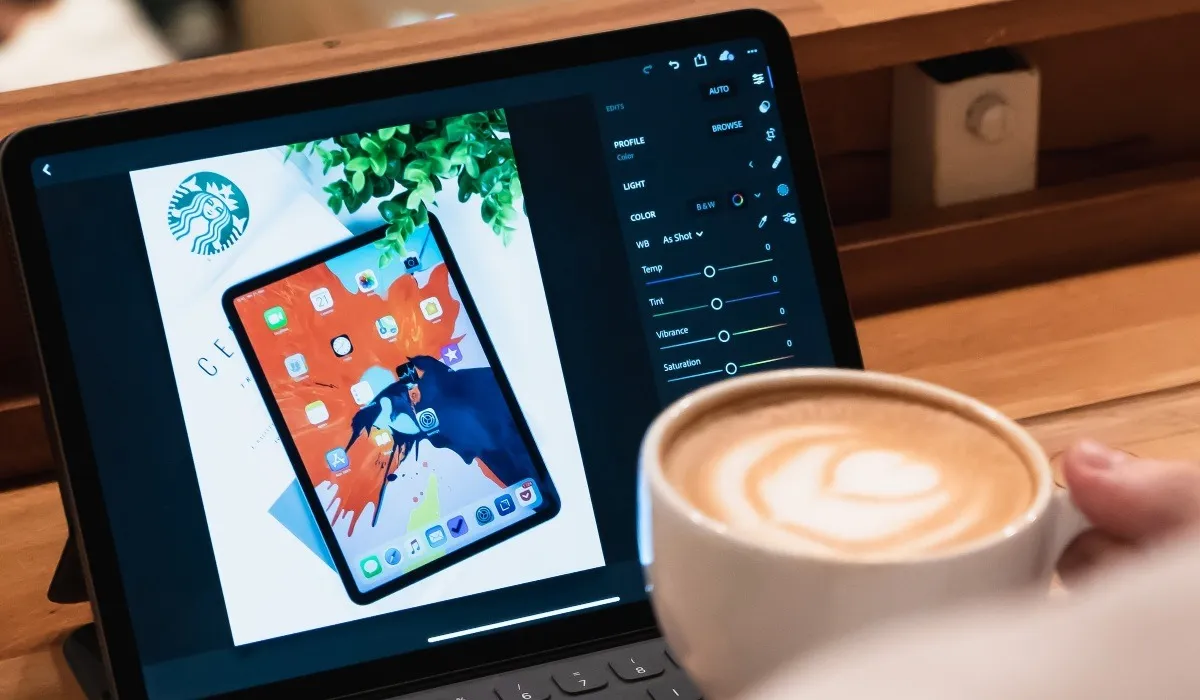 Person hält eine Kaffeetasse neben einem schwarzen iPad mit Tastatur