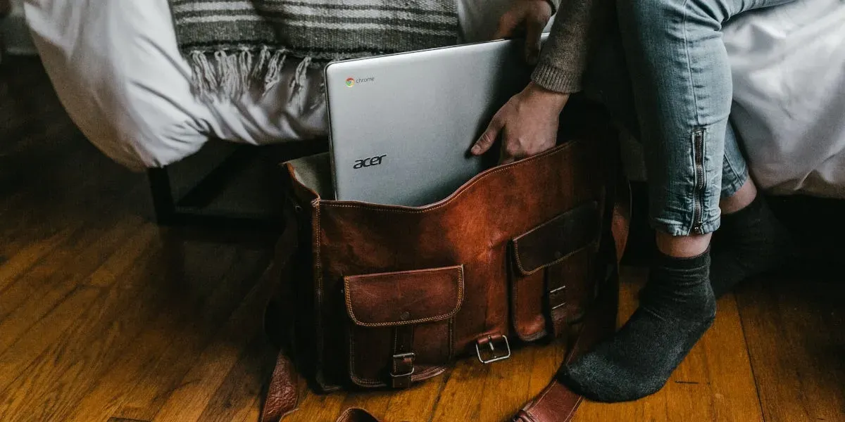 Adulto joven colocando una computadora portátil con batería en una bolsa antes de viajar