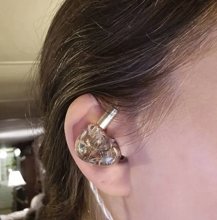 케이블이 귀 뒤에 꽂혀 있는 Kiwi Ears 인이어 모니터 헤드폰을 착용하고 있습니다.
