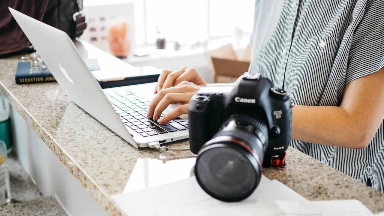 Una fotografia che mostra una persona su un laptop con una fotocamera al suo fianco.