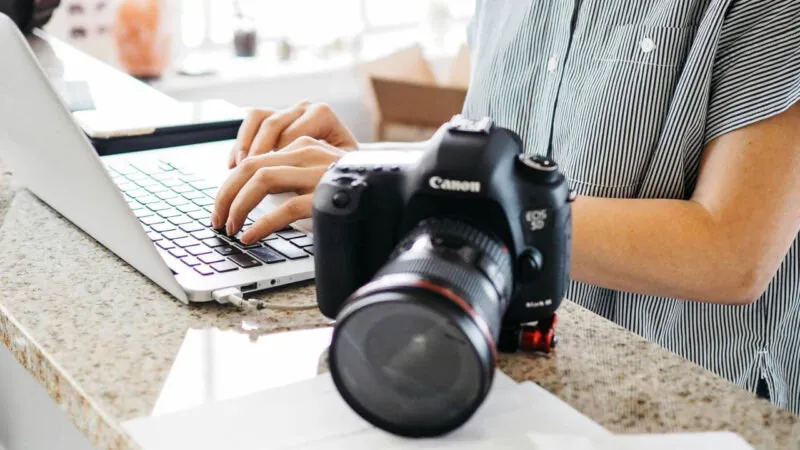 Uma fotografia de uma pessoa digitando em um laptop ao lado de uma câmera SLR.