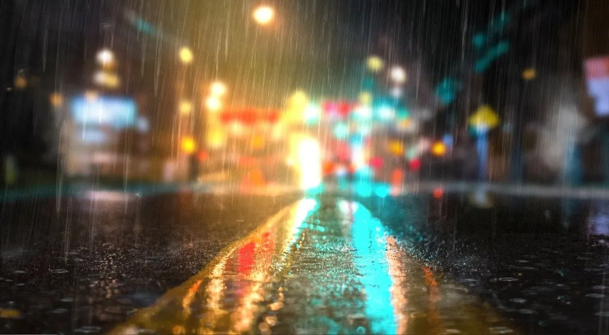 Chuva caindo em uma estrada de concreto com luzes difusas ao fundo