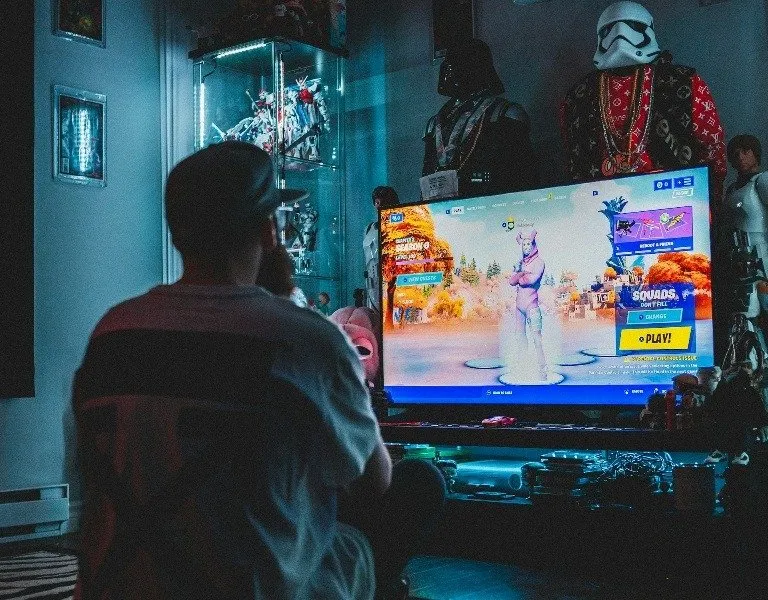 Mann sitzt und spielt ein Spiel auf einem Fernseher mit mehreren Figuren im Hintergrund