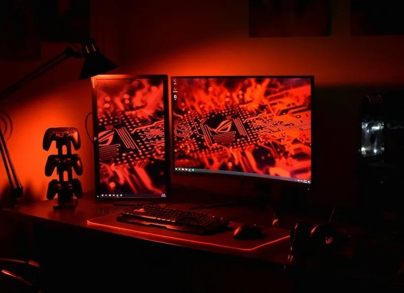 붉은빛으로 물든 책상 위에 놓인 게임용 PC와 듀얼 모니터