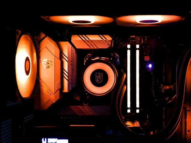 Close-up van een gaming-pc met een CPU-koeler, RAM en ventilatoren in oranje verlichting
