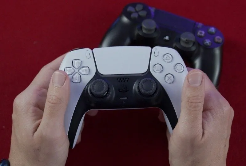 Persoon die een PlayStation 5-controller vasthoudt met een PlayStation 4-controller op de achtergrond